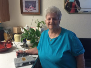 Listener Birdie Knapp with her digital receiver in her home, smiling and looking content.