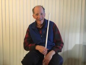 Weinberg sits in a room holding a white cane and smiling.