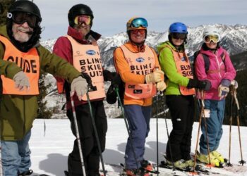 5 skiers posing,wearing "blind skier" and "guide" vests