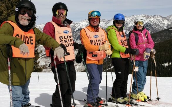 5 skiers posing,wearing "blind skier" and "guide" vests