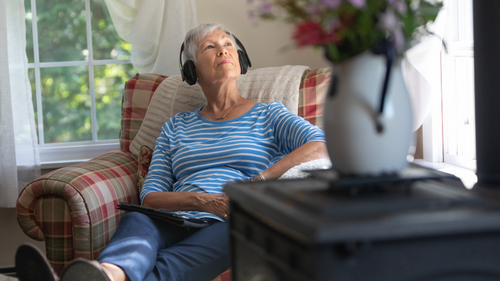 Senior woman listening to headphones on a chair in a living room.