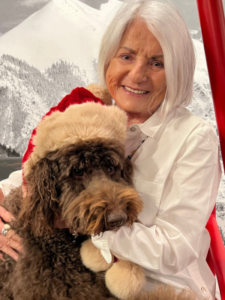 Carol smiling holding a dog that's wearing a santa hat.