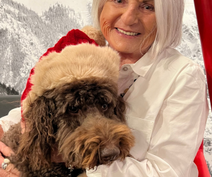 Carol smiling holding a dog that's wearing a santa hat.