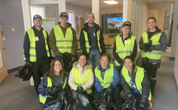 9 people posing in bright vests, gloves, and holding trash bags.