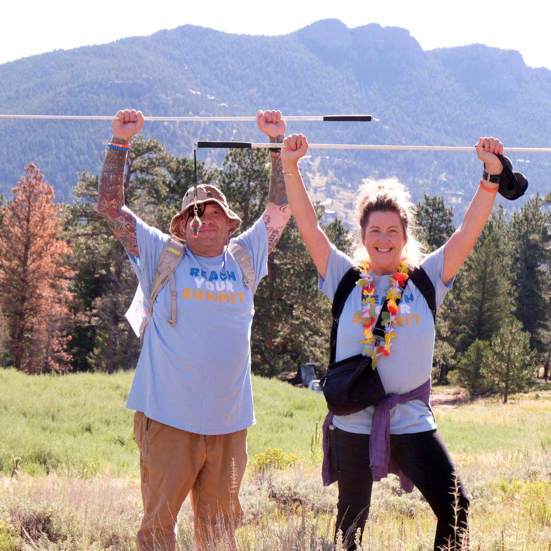 Two hikers in a mountain scene holding up white canes, smiling